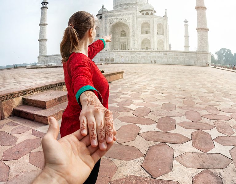 Woman in red Indian costume holding man by hand and pointing to Taj Mahal in Agra, Uttar Pradesh, India